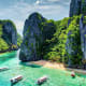 Turquoise lagoon surrounded by towering limestone cliffs and lush vegetation with traditional boats and beachgoers in Philipp